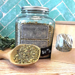 Jar of 'Afternoon Delight Tea' with a wooden scoop and packaging on a tiled background. Herbal apothecary near DuBois Pa.