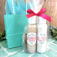Two bottles of body lotion with a pink bow and a turquoise gift bag on a tiled floor. Birthday gift ideas. Birthday gift shop DuBois Pa.