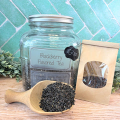 Glass jar of blackberry flavored tea with wooden scoop and packaging on a wooden surface. Black teas. Loose leaf teas.