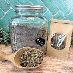 Glass jar of bladder support tea with a wooden scoop and packaging on a wooden surface. Herbs for bladder support. Teas to support bladder health.