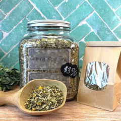 Jar of 'Calming Rest Tea' with a wooden scoop and packaging on a tiled background. Herbal tea blend for relaxing and calming.