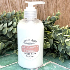 Goats milk lotion bottle with pump on a tiled surface with greenery in the background