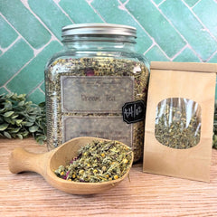 Jar of 'Dream Tea' with a wooden scoop and packaging on a wooden surface with a teal tiled wall background. Teas for relaxation. Teas for sleep. Tea for sleeping.