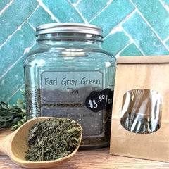 Glass jar of Earl Grey Green Tea with a small wooden spoonful of tea leaves on a wooden surface. Favorite Green Teas .  Benefits of green teas.