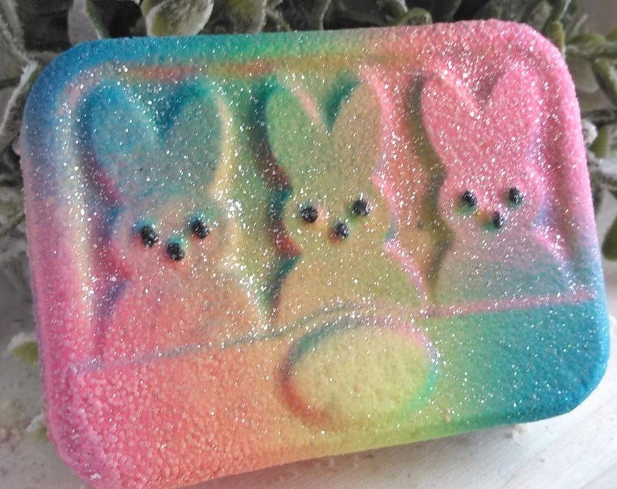 Flat lay of a bath bomb featuring three Easter peep bunny shapes. Airbrushed with the colors of pink, blue, and yellow.