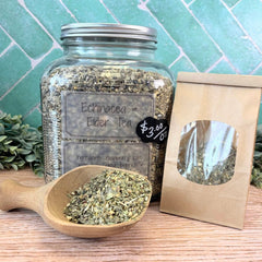 Jar of Echinacea Elder Tea with a wooden scoop and packaging on a wooden surface with a green tiled background. Herbs for immunity.