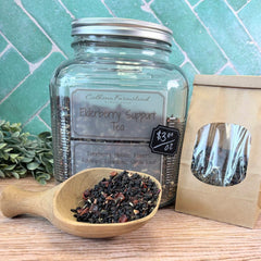 Glass jar of elderberry support tea with a wooden scoop and packaging on a wooden surface. Herbs for boosting immunity naturally. 