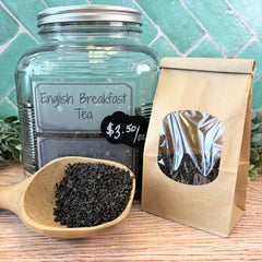 Glass jar of English Breakfast Tea with a paper bag and wooden scoop on a tiled background. Breakfast tea.