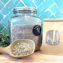 Glass jar withEssiac Tea, wooden spoon with tea leaves, and packaging on a tiled background. Alternative medicines. 