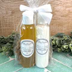 Two bottles of facial wash and lotion in clear cellophane with a white bow, on a wooden surface with greenery. Skin care gift sets. Skin care with natural ingredients.