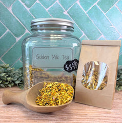 Glass jar labeled 'Golden Milk Tea' with a wooden scoop and paper bag on a wooden surface. Herbs for inflammation.