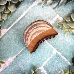 Gua sha brush on a textured surface with green leaves. Lymph moving facial masage