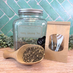Honey Ginseng Tea jar with wooden scoop and brown paper bag on a wooden surface with green tiled background. Herbs to improve memory.