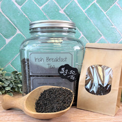 Glass jar of Irish Breakfast Tea with a wooden scoop and packaging on a tiled surface. Black teas in pennsylvania