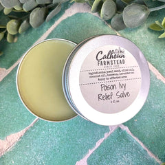 Calhoun Farmstead Poison Ivy Relief Salve in a metal tin on a green stone surface with leaves in the background.
