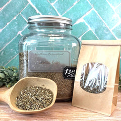 Jar of lemon balm with a wooden scoop and packaging on a tile background. Herbs for reducing stress and anxiety. Improve sleep quality.