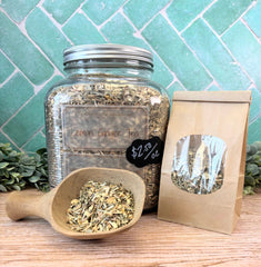 Jar of lemon ginger tea with a scoop and packaging on a wooden surface with a green tiled background. Teas for tummy issues.