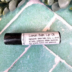 Lemon balm lip oil bottle on a textured green surface with leaves in the corner