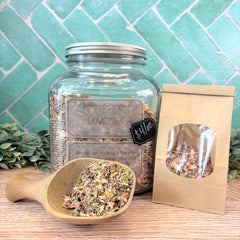 Glass jar of 'Love Tea' with a wooden scoop and packaging on a wooden surface with a teal tiled background. Herbal teas. Wellness store DuBois Pennsylvania.