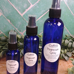 Three blue bottles of magnesium spray with labels on a wooden surface and green tiled background.