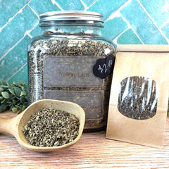 Jar of Mullein Leaf with a wooden scoop and packaging on a tiled background. Herbs for cough, colds, and mucus. 
