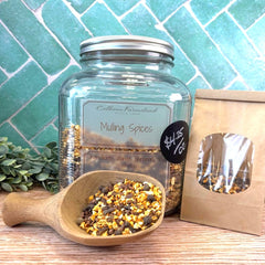 Glass jar of Mulling Spices with a wooden scoop and small packet on a tiled surface. Herbs for making mulled cider. Herbs for making mulled wine.