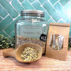 Glass jar with tea leaves, wooden scoop, and brown paper bag on a wooden surface with a tiled wall background. Herb store in DuBois Pennsylvania