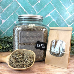 Glass jar labeled 'Raspberry Leaf' with a scoop of the product on a wooden surface against a tiled wall. background. Herbs for women. Teas for women.