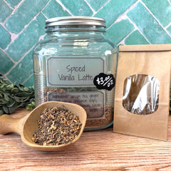 Spiced Vanilla Latte mix in a glass jar with a wooden scoop and packaging on a tiled background. Herbal apothecary located in DuBois Pa.