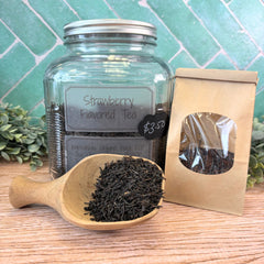 Glass jar of strawberry-flavored tea with a wooden scoop and packaging on a wooden surface. Flavored black tea. Morning tea. Summer tea.