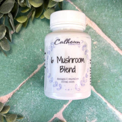 White supplement bottle labeled '6 Mushroom Blend' on a green leafy background