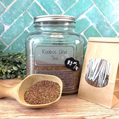 Jar of Rooibos Chai Tea with a scoop of tea and a paper bag on a wooden surface with a tiled background. Herbal tea. Spice tea. Chai tea.