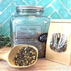 Glass jar of Rose Vanilla Echinacea Tea with a scoop of tea leaves on a wooden surface.