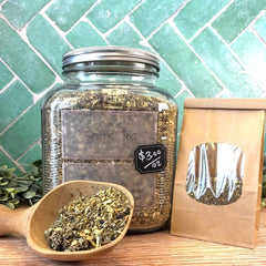 Glass jar of Sniffle Tea with a wooden scoop and tea bag on a wooden surface with a green tiled . Herbals for colds and flu. green background.