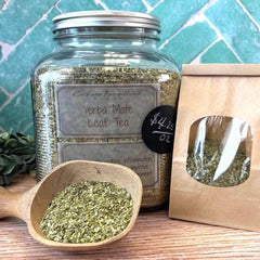 Jar of yerba mate leaf tea with a wooden scoop and packaging on a tiled background