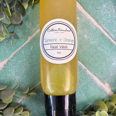 Yellow bottle of Calhoun Farmstead Turmeric & Orange Facial Wash on a green tiled background with leaves. Facial care with turmeric.