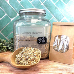 Jar of 'Winter's Remedy Tea' with a wooden scoop and packaging on a tiled background. Herbs for colds and flu. Herbs for cough and sore throats.