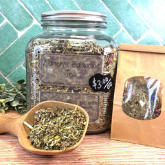 Glass jar of 'Women's Balancing Tea' with a wooden scoop and packaging on a tiled background. Herbs for women. Benefits of raspberry leaf for women's health.