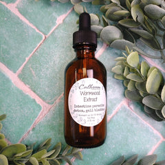 Brown glass bottle with dropper labeled 'Wormwood Extract' on a green tile background with plants.