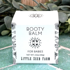 Box of Booty Balm for Babies by Little Seed Farm on a green surface with plants in the background. Booty Balm for diaper rash. Baby balm.