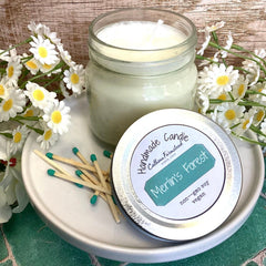 Handmade candle in a jar with a lid, surrounded by daisies on a wooden surface.