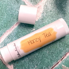 Lip balm tube labeled 'Honey Tea' on a textured green background