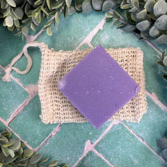 Purple soap bar on a textured mat with green leaves in the background